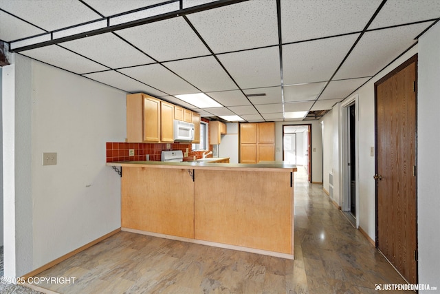 kitchen with light wood-type flooring, a drop ceiling, tasteful backsplash, a peninsula, and white microwave