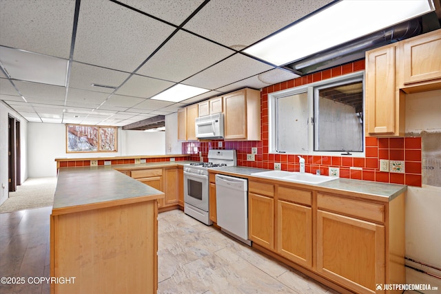 kitchen with a sink, white appliances, tasteful backsplash, and a peninsula