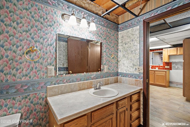 bathroom featuring wood finished floors, vanity, and wallpapered walls