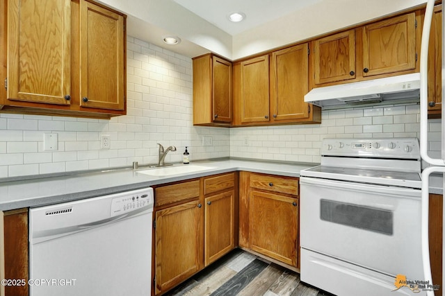 kitchen with under cabinet range hood, decorative backsplash, brown cabinets, white appliances, and a sink