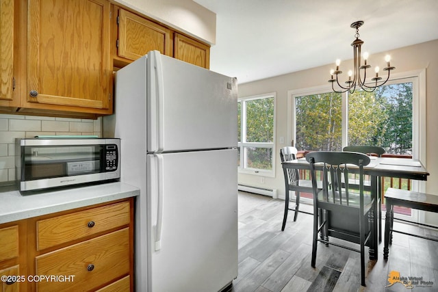 kitchen featuring brown cabinets, backsplash, freestanding refrigerator, a baseboard radiator, and a chandelier