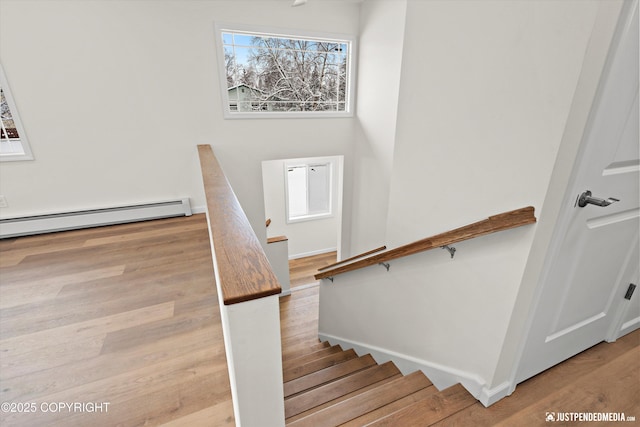 stairway featuring baseboard heating, baseboards, and wood finished floors