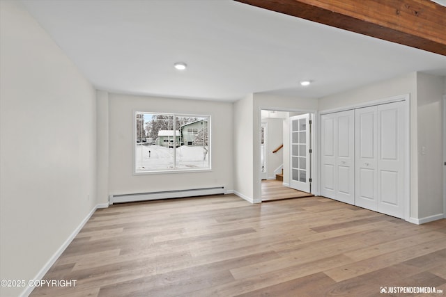 unfurnished bedroom featuring a closet, light wood-style flooring, a baseboard heating unit, and baseboards