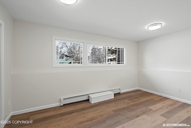 spare room featuring a baseboard radiator, baseboards, and wood finished floors