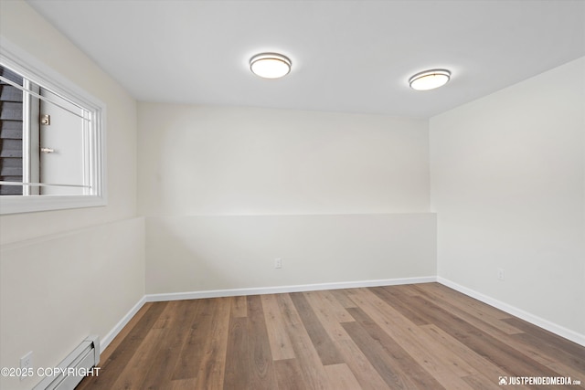 empty room with a baseboard heating unit, baseboards, and wood finished floors