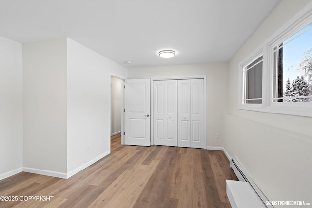 unfurnished bedroom featuring a baseboard heating unit, wood finished floors, baseboards, and a closet