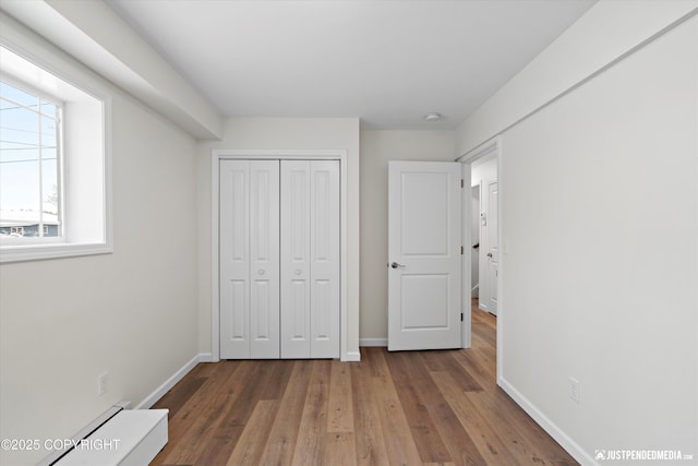 unfurnished bedroom with a closet, a baseboard heating unit, baseboards, and wood finished floors