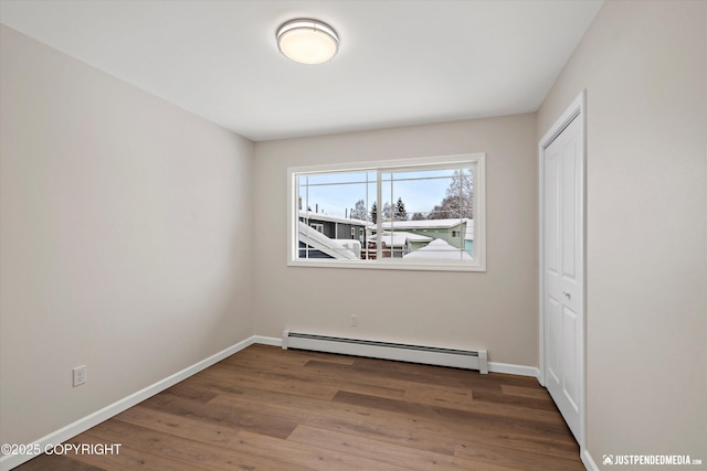 unfurnished bedroom featuring a closet, baseboard heating, baseboards, and wood finished floors