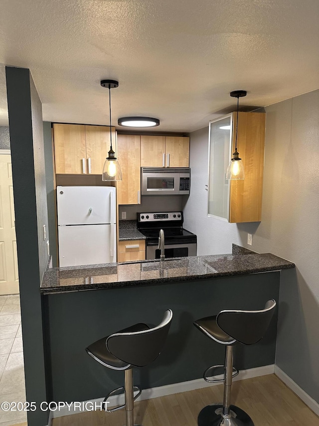 kitchen featuring dark stone countertops, a kitchen bar, a textured ceiling, and appliances with stainless steel finishes