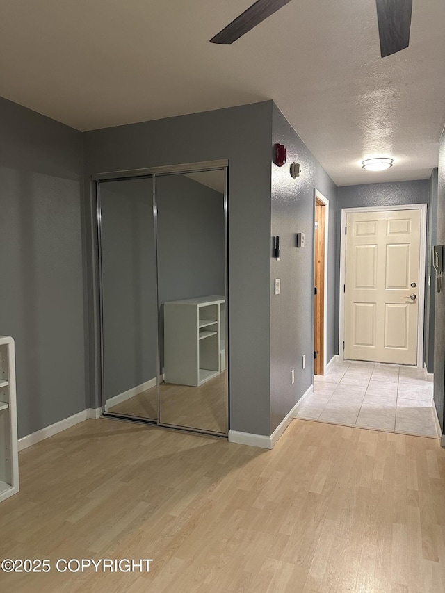 hallway with baseboards, a textured ceiling, and light wood-style flooring