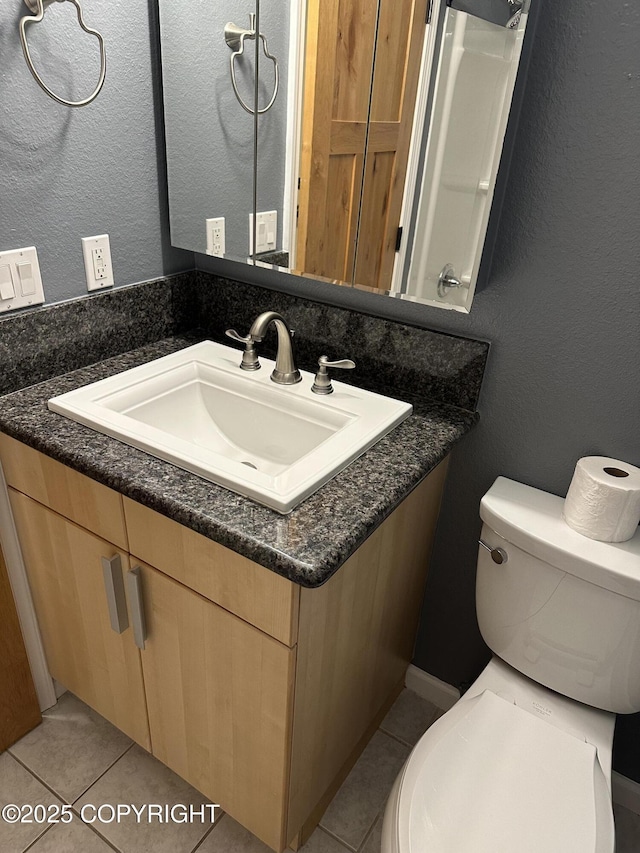 bathroom with tile patterned floors, toilet, vanity, and a textured wall