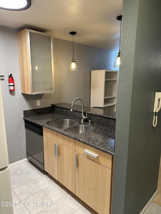 kitchen featuring light brown cabinetry, dishwasher, dark stone counters, hanging light fixtures, and a sink