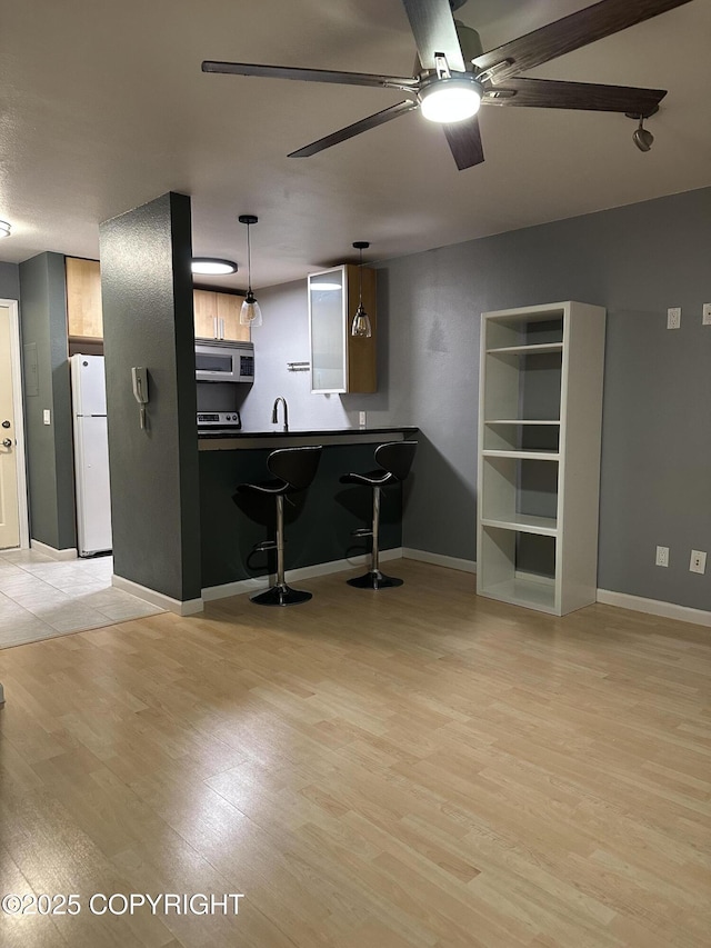 kitchen featuring dark countertops, stainless steel microwave, freestanding refrigerator, light wood-style floors, and a ceiling fan