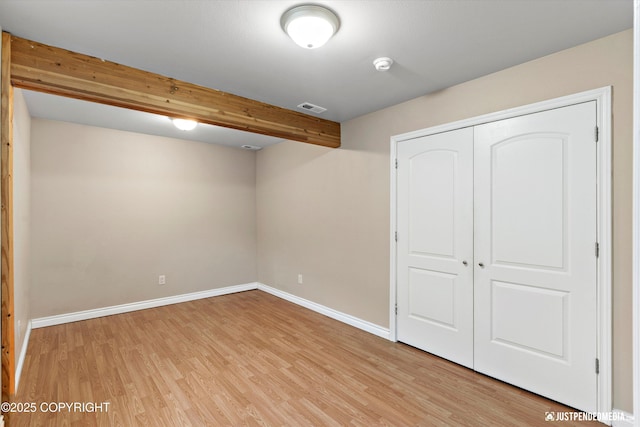 unfurnished bedroom featuring beam ceiling, light wood-style floors, visible vents, and baseboards