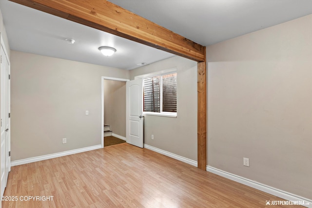 unfurnished room with light wood finished floors, beamed ceiling, visible vents, and baseboards