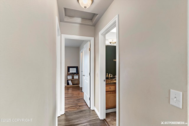 hall with attic access, dark wood-type flooring, baseboards, and a raised ceiling