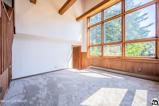 empty room featuring beam ceiling, a baseboard heating unit, carpet floors, wooden walls, and a towering ceiling