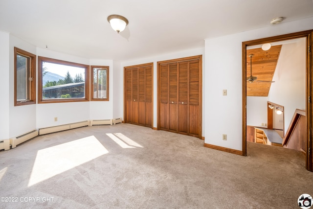 unfurnished bedroom featuring carpet flooring, baseboards, multiple closets, and a baseboard radiator