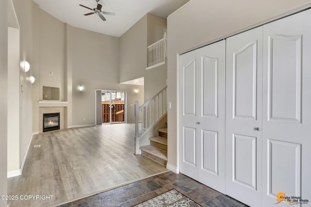 1091 Northpointe Bluff Dr, Anchorage, AK 99501 - unfurnished living room with ceiling fan, a high ceiling, stairs, a glass covered fireplace, and wood finished floors