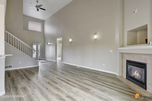 1091 Northpointe Bluff Dr, Anchorage, AK 99501 - unfurnished living room featuring high vaulted ceiling, a ceiling fan, a glass covered fireplace, stairs, and wood finished floors