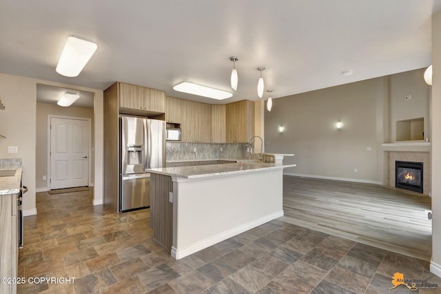 1091 Northpointe Bluff Dr, Anchorage, AK 99501 - kitchen featuring stainless steel fridge, backsplash, light stone counters, light brown cabinetry, and a glass covered fireplace