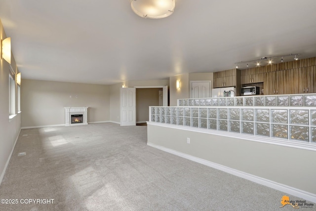 1091 Northpointe Bluff Dr, Anchorage, AK 99501 - unfurnished living room featuring light colored carpet, a lit fireplace, and rail lighting
