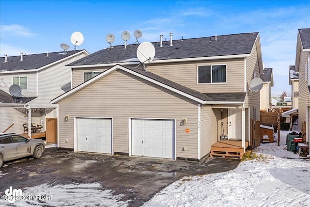 rear view of property with a garage, roof with shingles, and driveway