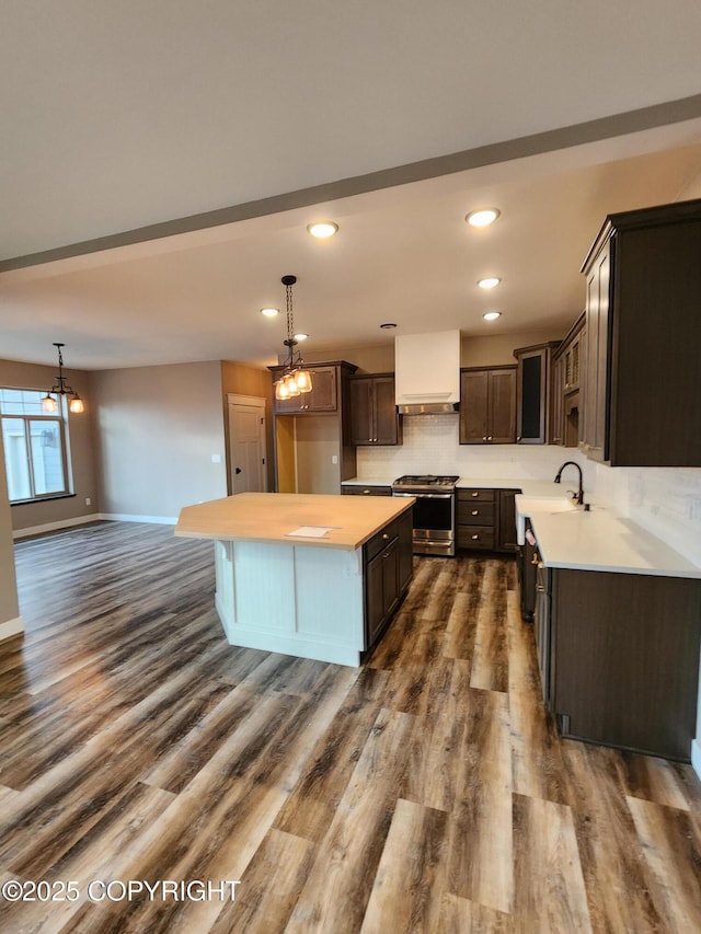 kitchen featuring dark brown cabinets, dark wood finished floors, light countertops, decorative backsplash, and stainless steel gas range