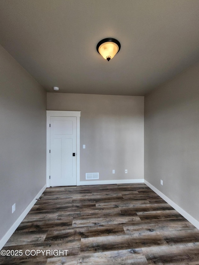 spare room with visible vents, baseboards, and dark wood-type flooring