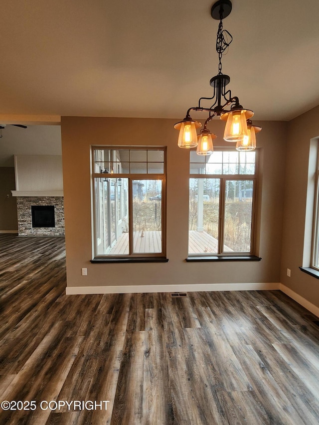 unfurnished dining area featuring a stone fireplace, visible vents, baseboards, and wood finished floors