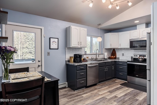 kitchen with a sink, a baseboard heating unit, white cabinetry, appliances with stainless steel finishes, and lofted ceiling