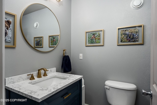 bathroom with toilet, vanity, and a textured wall