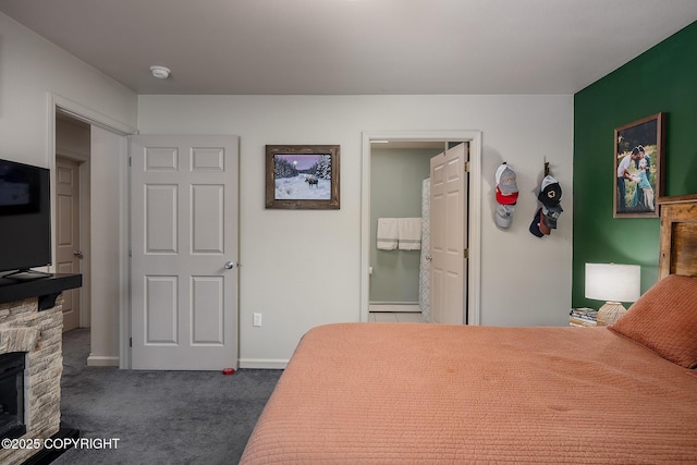 bedroom featuring a stone fireplace, dark carpet, baseboards, and a baseboard radiator