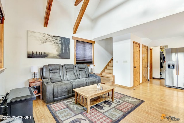 living area with light wood-style flooring, high vaulted ceiling, stairs, and baseboards