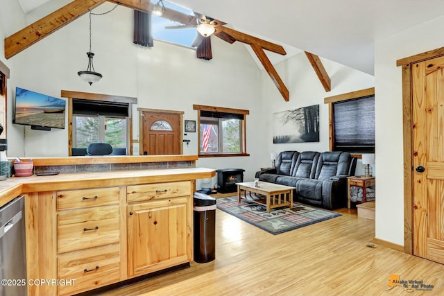 kitchen with open floor plan, beamed ceiling, dishwasher, a wood stove, and light wood-style floors