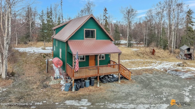 view of front of home featuring a porch, metal roof, and a forest view