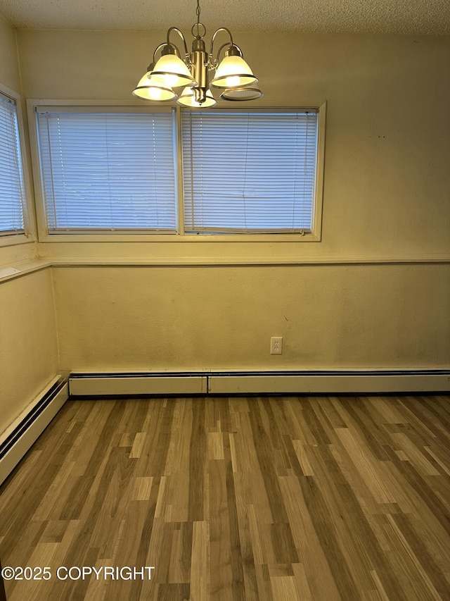 spare room with a notable chandelier, baseboard heating, wood finished floors, and a textured ceiling