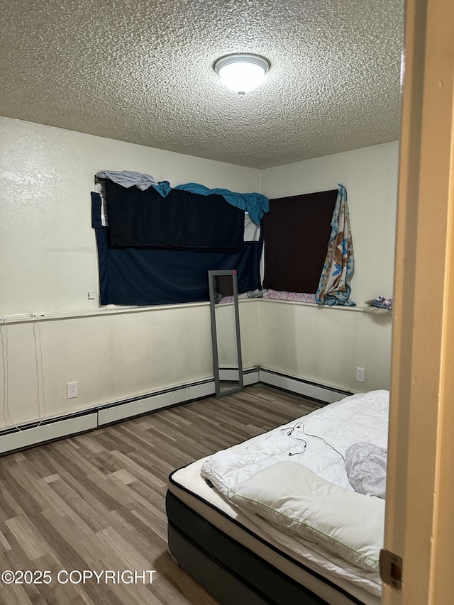 bedroom featuring a baseboard heating unit, wood finished floors, and a textured ceiling