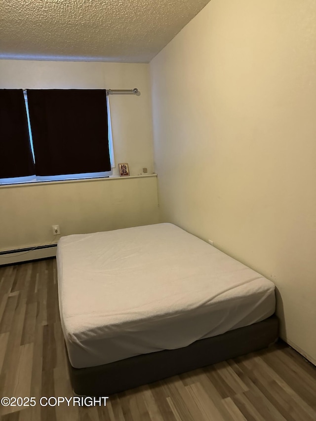 unfurnished bedroom featuring baseboard heating, a textured ceiling, and wood finished floors