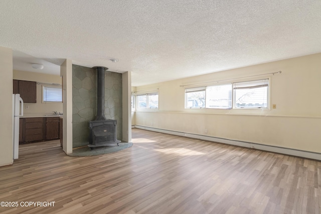 2752 W 42nd Ave Unit 4, Anchorage, AK 99517 - unfurnished living room featuring a textured ceiling, a wood stove, wood finished floors, a baseboard radiator, and a sink