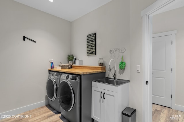 washroom with a sink, baseboards, washing machine and dryer, and light wood finished floors