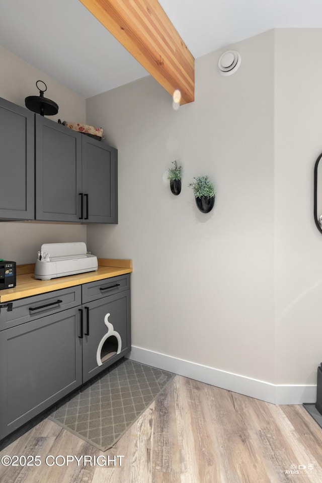 kitchen featuring beam ceiling, gray cabinetry, light wood-style floors, light countertops, and baseboards