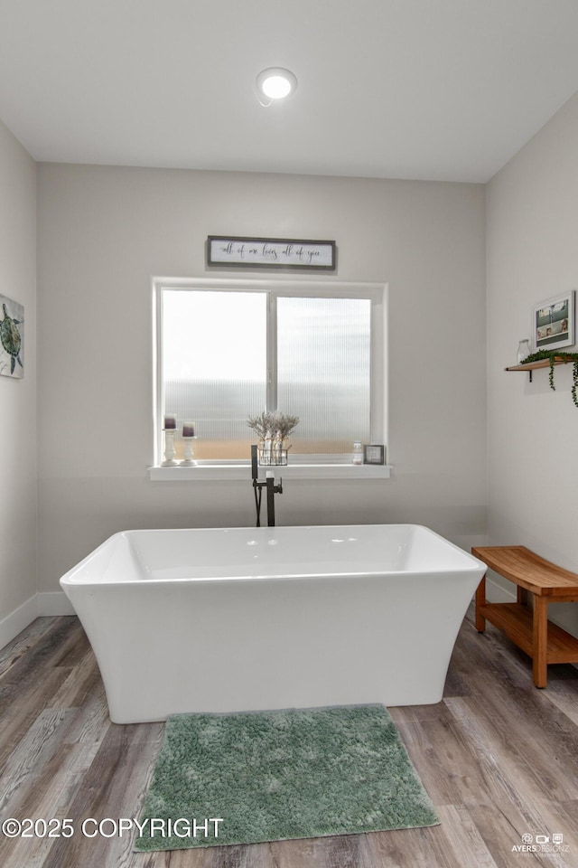 full bathroom with a freestanding tub, baseboards, and wood finished floors