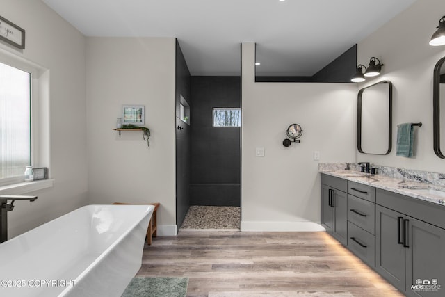 full bathroom with wood finished floors, baseboards, double vanity, a freestanding tub, and a sink