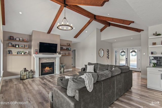 living area featuring beam ceiling, light wood-style flooring, high vaulted ceiling, and an inviting chandelier