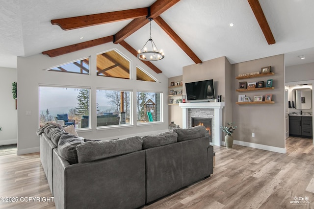 living area featuring baseboards, beam ceiling, a fireplace, an inviting chandelier, and light wood-style floors