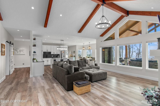 living area featuring a chandelier, beamed ceiling, light wood-style floors, and a barn door