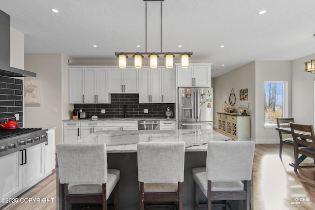 kitchen with light wood-type flooring, white cabinetry, stainless steel appliances, wall chimney exhaust hood, and decorative backsplash