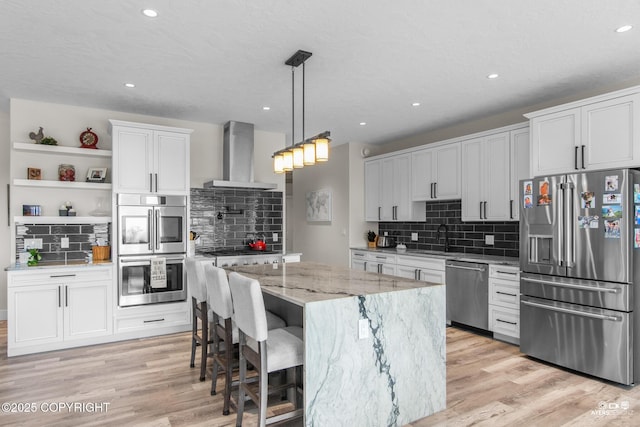 kitchen featuring appliances with stainless steel finishes, wall chimney exhaust hood, light wood-style floors, and a sink