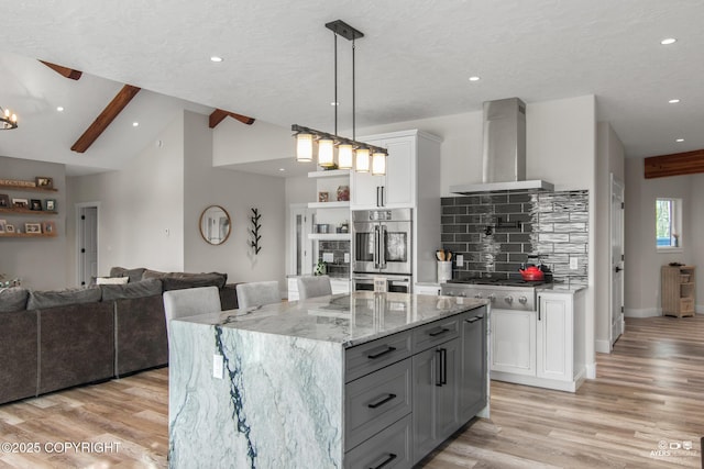 kitchen with appliances with stainless steel finishes, white cabinetry, wall chimney range hood, open floor plan, and backsplash